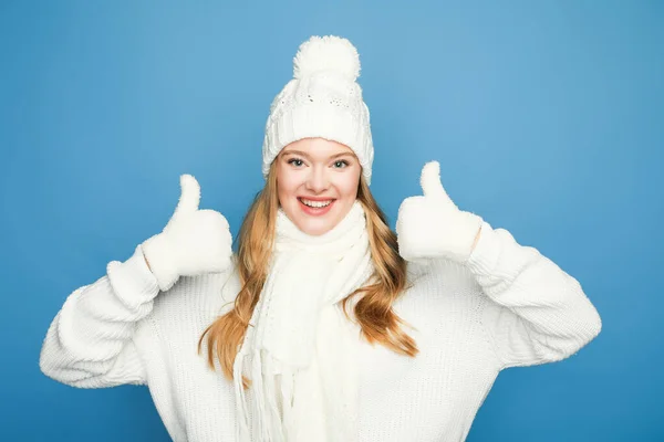 Feliz rubia hermosa mujer en invierno blanco traje mostrando pulgares hacia arriba sobre fondo azul - foto de stock