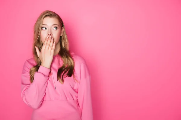 Потрясенная красивая женщина, прикрывающая рот на розовом фоне — стоковое фото
