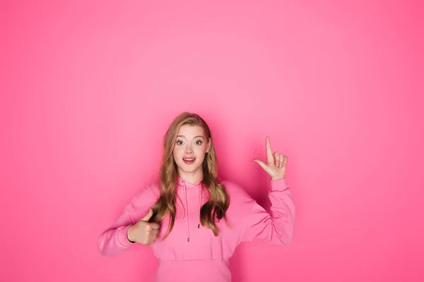 Sorridente bella donna che punta con il dito e mostrando pollice su sfondo rosa — Foto stock