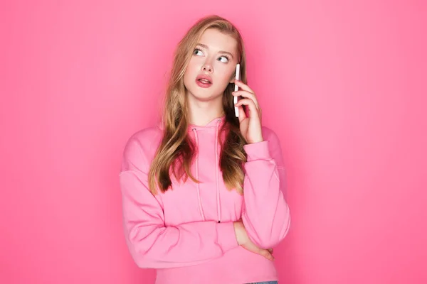 Стомлена красива жінка говорить на смартфоні на рожевому фоні — стокове фото