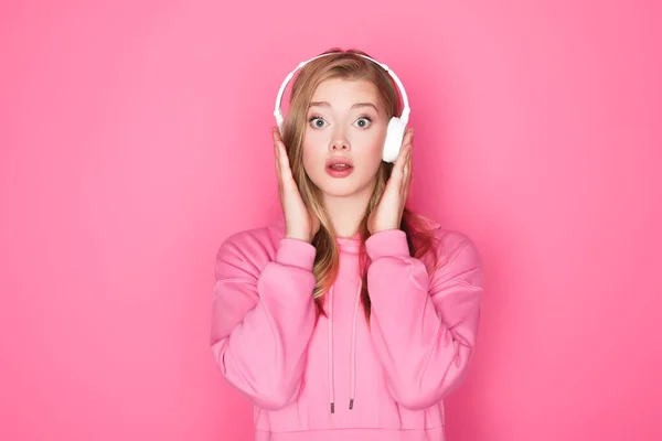 Schockierte schöne Frau hört Musik über Kopfhörer auf rosa Hintergrund — Stockfoto