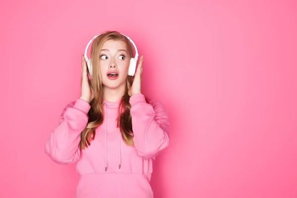 Choqué belle femme écouter de la musique dans les écouteurs sur fond rose — Photo de stock