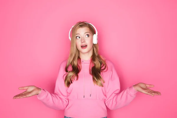 Schockierte schöne Frau hört Musik über Kopfhörer auf rosa Hintergrund — Stockfoto