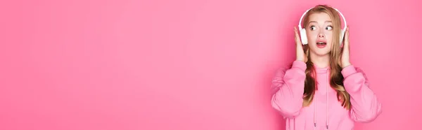 Shocked beautiful woman listening music in headphones on pink background, banner — Stock Photo