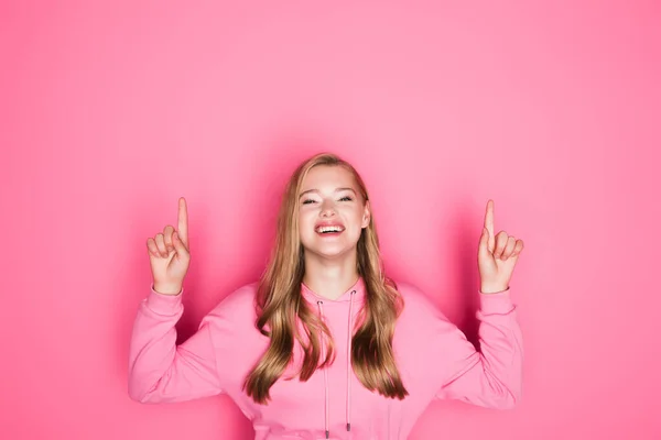 Glücklich schöne junge Frau im Kapuzenpulli zeigt Daumen nach oben auf rosa Hintergrund — Stockfoto