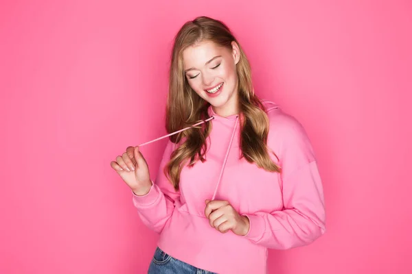 Beautiful young woman in hoodie smiling on pink background — Stock Photo