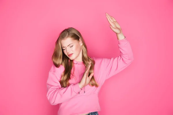 Beautiful young woman in hoodie showing stop gesture on pink background — Stock Photo