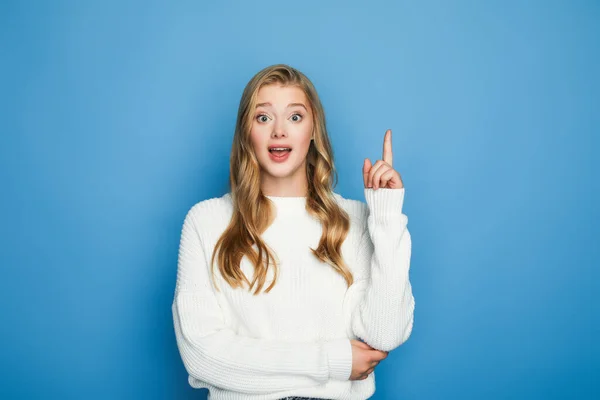 Excited blonde beautiful woman in sweater showing idea gesture isolated on blue — Stock Photo