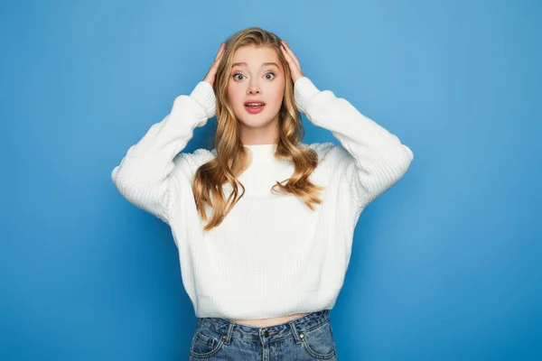 Shocked blonde beautiful woman in sweater holding head isolated on blue — Stock Photo