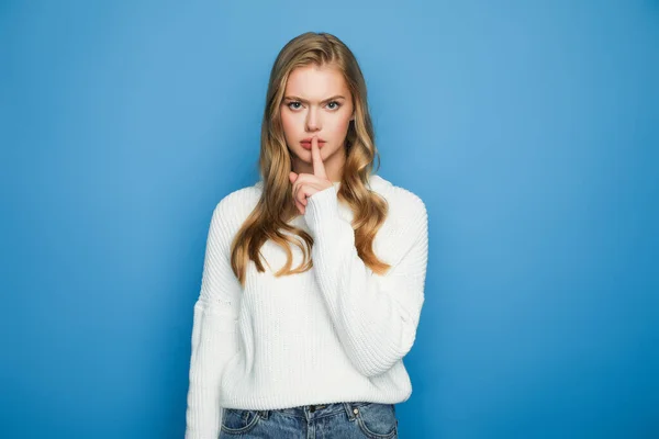 Tenso loira bela mulher em suéter mostrando shh isolado no fundo azul — Fotografia de Stock