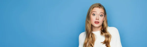 Surprised blonde beautiful woman in sweater isolated on blue background, banner — Stock Photo