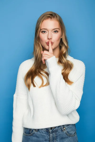 Blonde beautiful woman in sweater showing shh isolated on blue background — Stock Photo