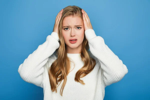 Triste bionda bella donna in maglione tenendo la testa isolata su sfondo blu — Foto stock