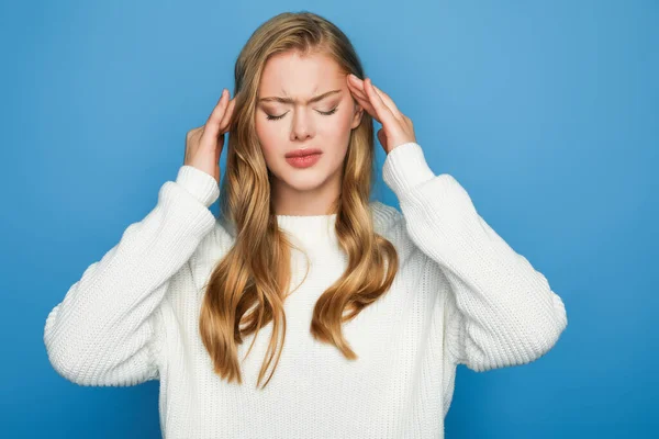 Blonde beautiful woman in sweater having headache isolated on blue background — Stock Photo