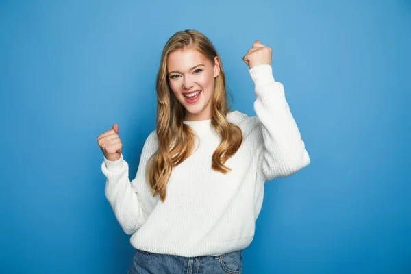 Felice bella donna bionda in maglione mostrando sì gesto isolato su sfondo blu — Foto stock