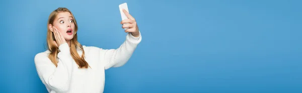 Impactado rubia hermosa mujer tomando selfie aislado sobre fondo azul, pancarta - foto de stock