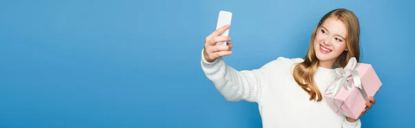 Blonde belle femme en pull prenant selfie avec boîte cadeau isolé sur bleu, bannière — Photo de stock