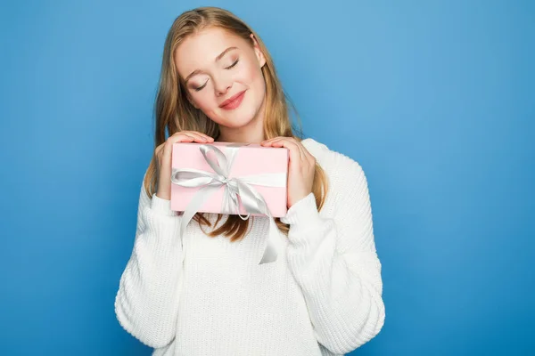 Erfreut blonde schöne Frau im Pullover mit Geschenkschachtel isoliert auf blau — Stockfoto