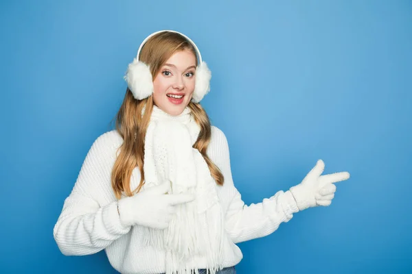 Souriant belle femme en tenue blanche d'hiver pointant de côté isolé sur bleu — Photo de stock