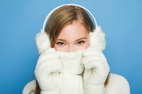 Hermosa mujer en invierno traje blanco cubriendo la cara con bufanda aislada en azul - foto de stock