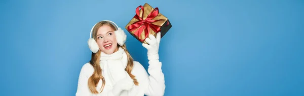 Lächelnde schöne Frau im winterweißen Outfit mit Geschenkbox isoliert auf blau, Banner — Stockfoto