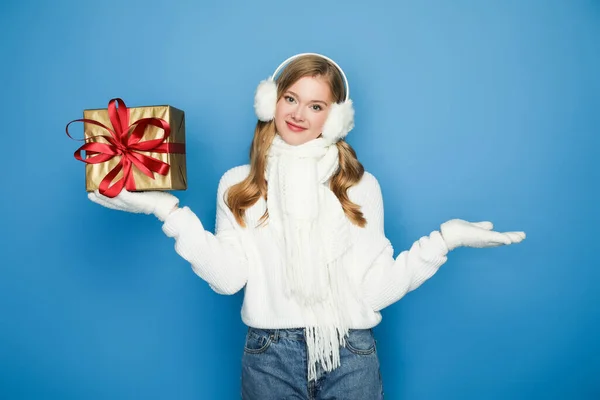 Lächelnd schöne Frau im winterweißen Outfit mit Geschenkbox isoliert auf blau — Stockfoto