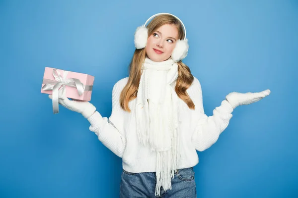 Smiling beautiful woman in winter white outfit with gift box isolated on blue — Stock Photo