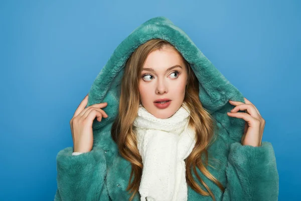 Mujer con estilo en abrigo de piel sintética verde mirando hacia otro lado aislado en azul - foto de stock