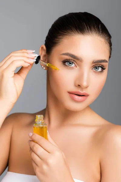 Woman applying serum on face isolated on grey — Stock Photo