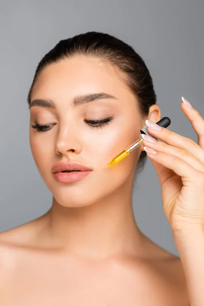 Femme appliquant du sérum sur le visage isolé sur le gris — Photo de stock