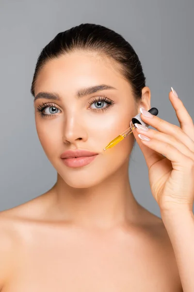 Naked woman applying serum on face isolated on grey — Stock Photo