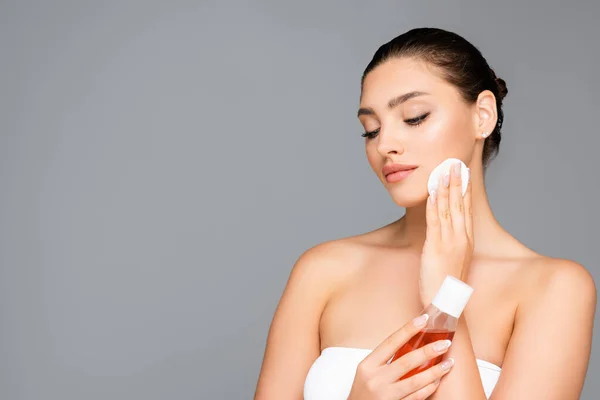 Belle femme avec bouteille de lotion et coton isolé sur gris — Photo de stock