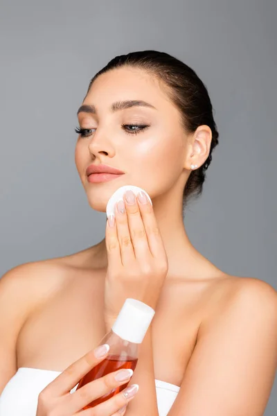 Beautiful woman with cotton pad and lotion isolated on grey — Stock Photo