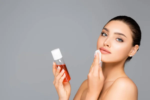 Beautiful woman with cotton pad and lotion isolated on grey — Stock Photo