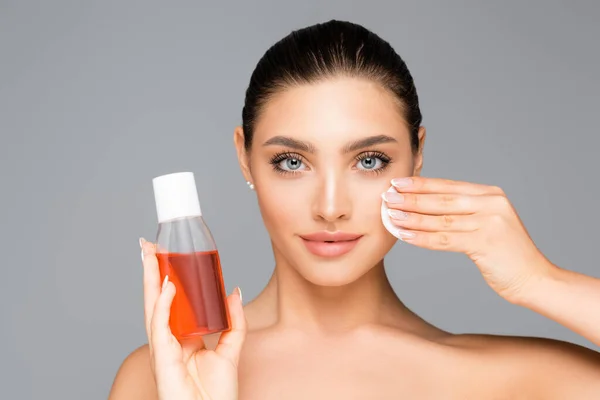 Beautiful woman with cotton pad and lotion isolated on grey — Stock Photo