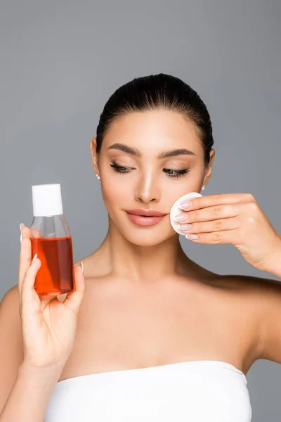 Beautiful woman with cotton pad and lotion isolated on grey — Stock Photo