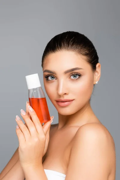 Hermosa mujer con botella de loción aislada en gris — Stock Photo