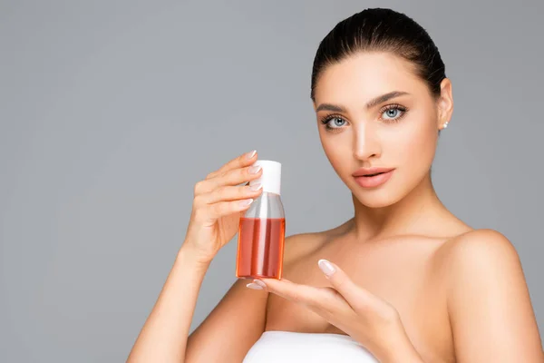 Hermosa mujer con botella de loción aislada en gris - foto de stock