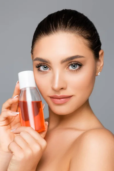 Belle femme avec bouteille de lotion isolée sur gris — Photo de stock