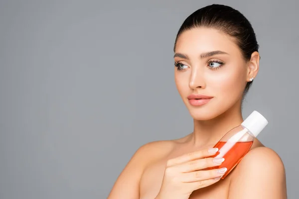 Beautiful woman with bottle of lotion isolated on grey — Stock Photo