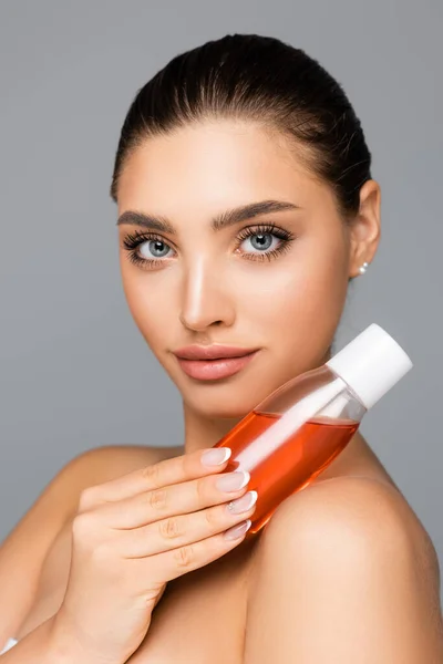 Hermosa mujer con botella de loción aislada en gris - foto de stock