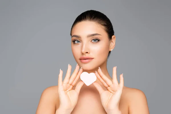 Femme avec épaules nues et éponge cosmétique en forme de coeur isolé sur gris — Photo de stock