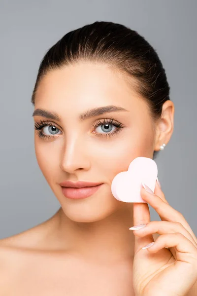 Woman with naked shoulders and heart shaped cosmetic sponge isolated on grey — Stock Photo