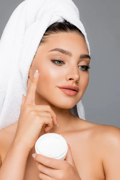 Femme avec serviette sur la tête appliquer crème cosmétique sur le visage isolé sur gris — Photo de stock