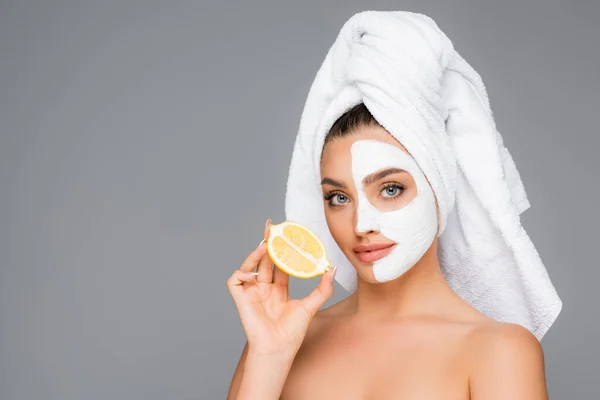 Woman with towel on head and clay mask on face holding lemon isolated on grey — Stock Photo