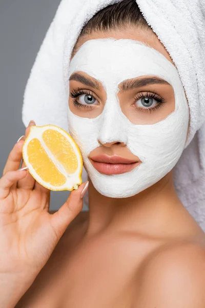 Woman with towel on head and clay mask on face holding lemon isolated on grey — Stock Photo