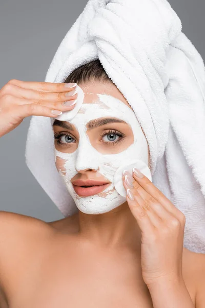 Femme avec serviette sur la tête rinçant masque d'argile sur le visage avec des tampons de coton isolé sur gris — Photo de stock