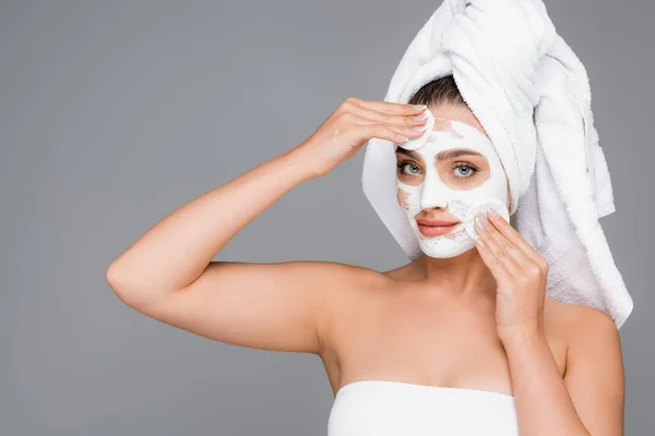 Femme avec serviette sur la tête rinçant masque d'argile sur le visage avec des tampons de coton isolé sur gris — Photo de stock