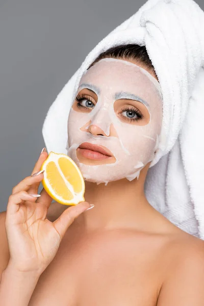 Woman with towel on head and mask sheet on face holding lemon isolated on grey — Stock Photo