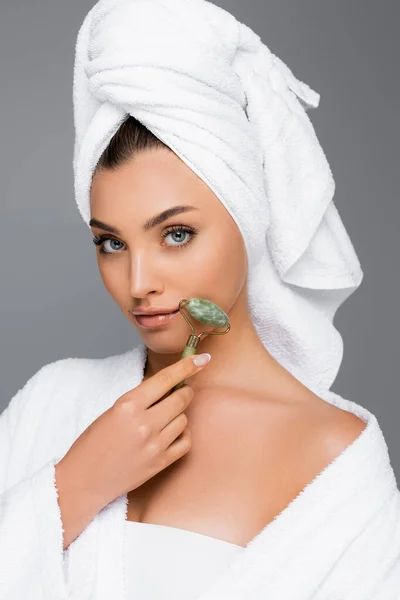 Frau mit Handtuch auf dem Kopf mit Jade-Rolle im Gesicht isoliert auf grau — Stockfoto